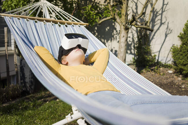 Fille couchée dans un hamac dans le jardin portant des lunettes VR — Photo de stock