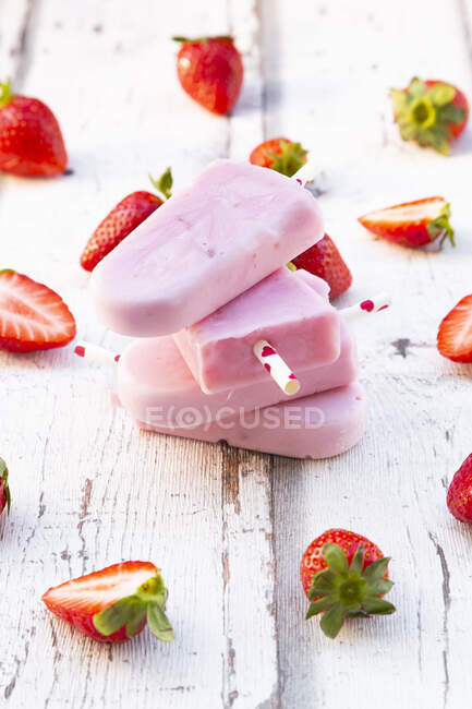 Stacked homemade strawberry yogurt ice lollies with fresh strawberries on white wood — Stock Photo