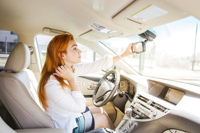 Business woman in a car checking her look in the rear-view mirror — Stock Photo