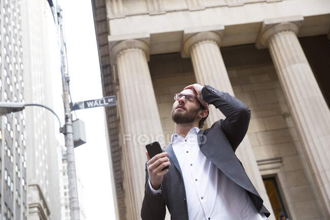 Portrait of worried young businessman with cell phone in front of Stock Exchange, New York City, USA — Stock Photo