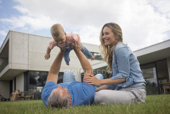 Счастливый отец с матерью поднимают маленькую девочку в сад — стоковое фото