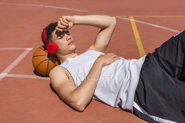 Young man lying on basketball, red headphones — Stock Photo