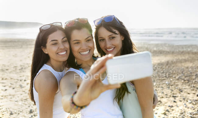 Portrait of happy female friends taking a selfie on the beach — Stock Photo