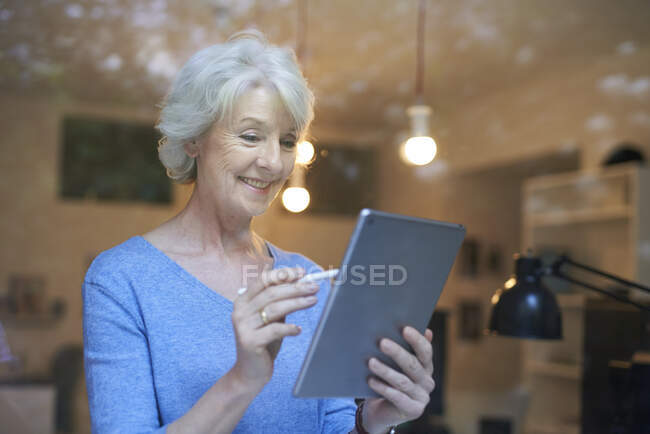 Портрет усміхненої зрілої жінки за вікном за допомогою цифрового планшета. — стокове фото