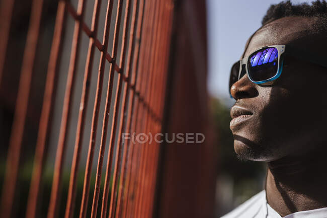 Серьезный молодой человек у забора в солнцезащитных очках — стоковое фото