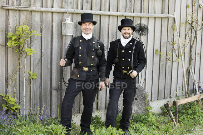 Портрет двух улыбающихся трубочистов, стоящих у деревянной стены — стоковое фото