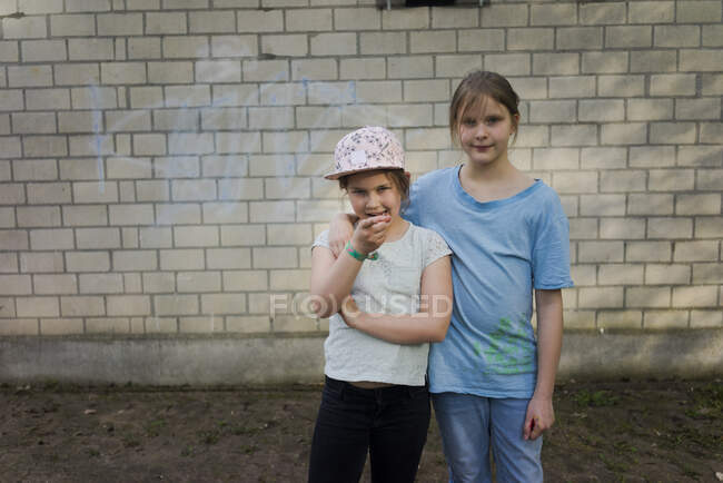 Retrato de dos niñas de pie frente a una pared de ladrillo - foto de stock