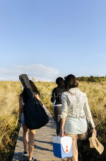 Rear view of women with guitar bag walking in dunes towards beach — Stock Photo