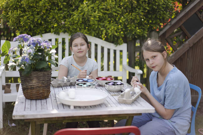 Portrait de deux filles teignant des œufs de Pâques sur une table de jardin — Photo de stock