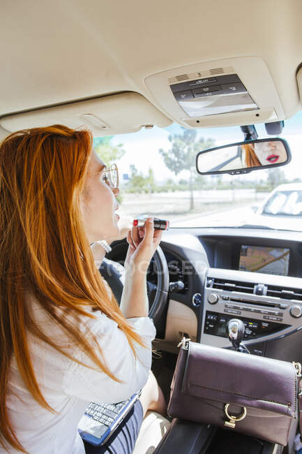 Mulher de negócios em um carro aplicando batom — Fotografia de Stock