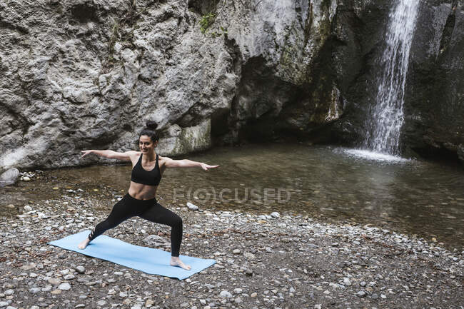 Женщина практикует йогу в водопаде, позирует воину — стоковое фото