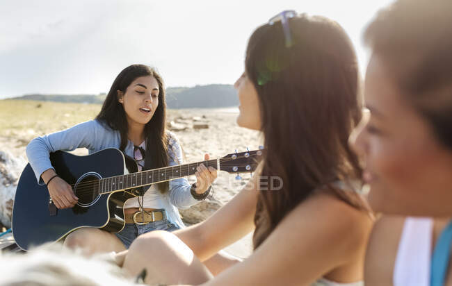 Giovane donna con amici che suonano la chitarra sulla spiaggia — Foto stock