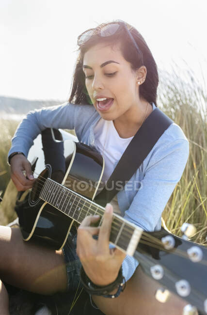 Giovane donna che canta e suona la chitarra sulla spiaggia — Foto stock