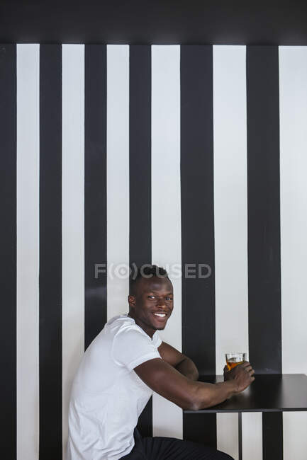 Portrait d'un jeune homme souriant assis à table avec un verre — Photo de stock