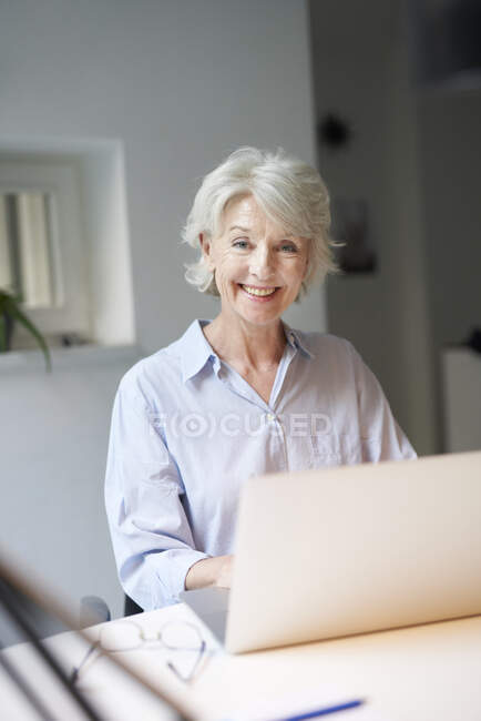 Portrait of smiling mature woman using laptop at desk — Stock Photo