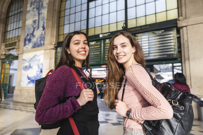 Ritratto di due giovani donne sorridenti con zaini in piedi davanti alla stazione, Porto, Portogallo — Foto stock