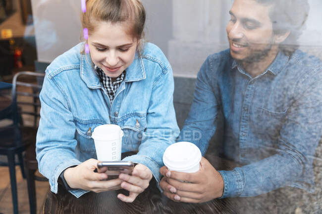 Young woman using smartphone in a coffee shop while her boyfriend watching her — Stock Photo