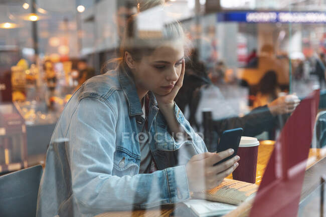 Jeune femme dans un café utilisant un smartphone — Photo de stock
