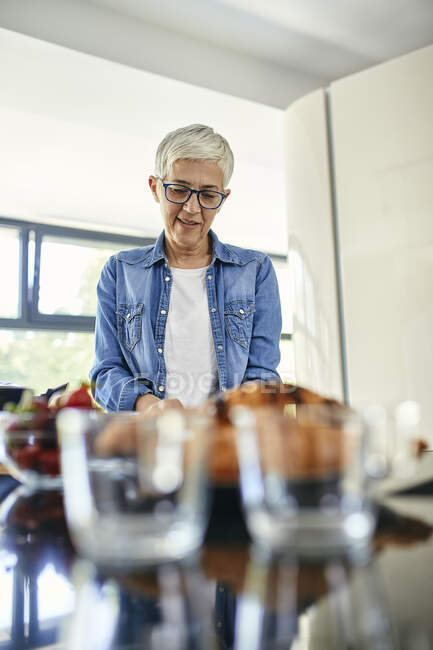 Femme âgée debout dans la cuisine, hachant des fraises — Photo de stock