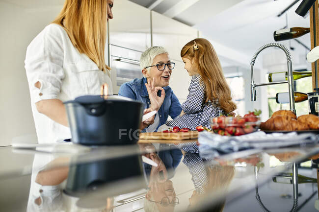 Mère, fille et grand-mère s'amusent, coupant des fraises dans la cuisine — Photo de stock