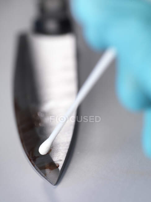 Científico forense tomando pruebas de ADN de un cuchillo manchado de sangre - foto de stock