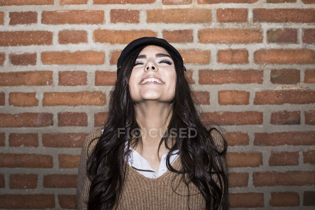 Portrait of smiling young woman with eyes closed in front of brick wall — Stock Photo