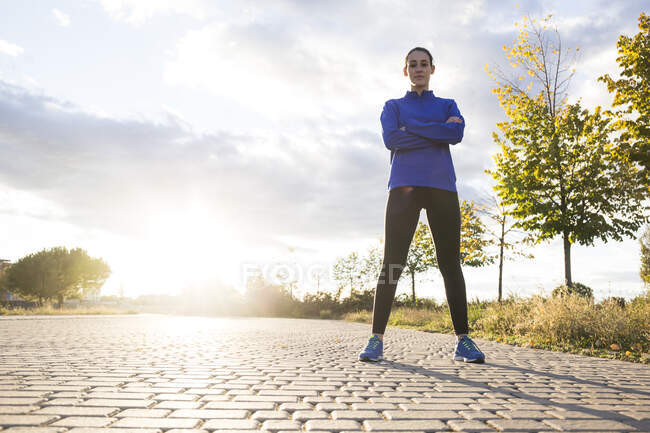 Young woman in sportswear posing in park with arms crossed, looking at camera — Stock Photo