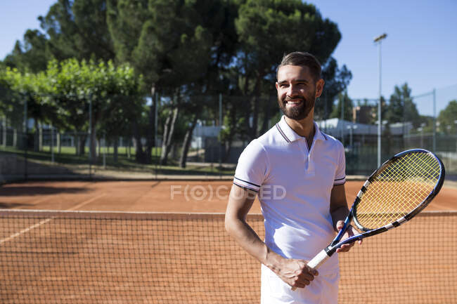 Привлекательный бородатый мужчина в теннисной одежде держит ракетку и смотрит в сторону — стоковое фото