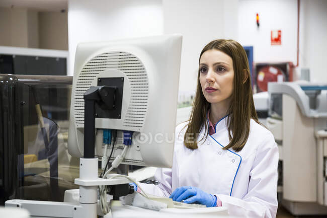 Jeune femme en vêtements blancs utilisant un analyseur d'échantillons tout en travaillant dans un laboratoire de recherche — Photo de stock