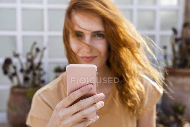 Рука посміхаючись почервоніла молода жінка тримає мобільний телефон, зблизька — стокове фото
