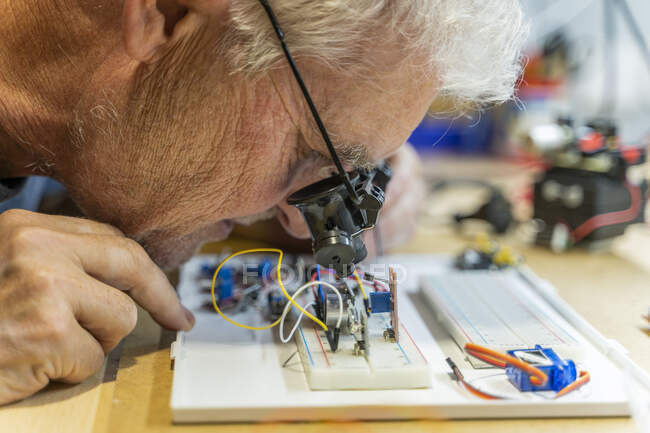 Hombre mayor trabajando en circuitos electrónicos en su taller - foto de stock