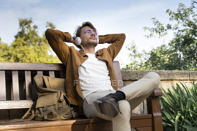 Mann sitzt auf Bank und hört Musik mit Kopfhörern — Stockfoto