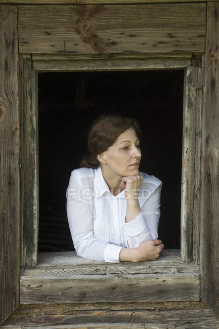 Mujer mirando por la ventana de una vieja casa de madera - foto de stock