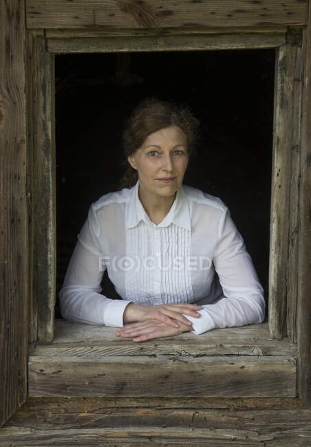 Портрет женщины, выглядывающей из окна старого деревянного дома — стоковое фото