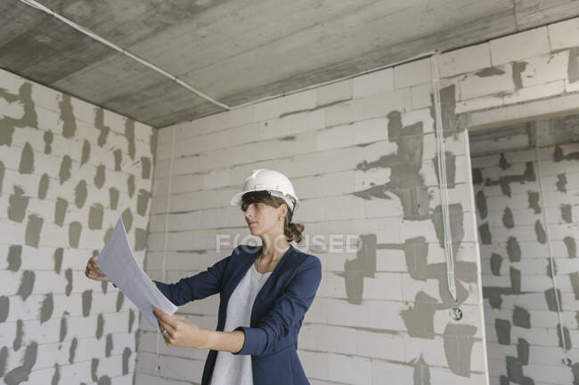 Female architect checking architectural plan on construction site — Stock Photo