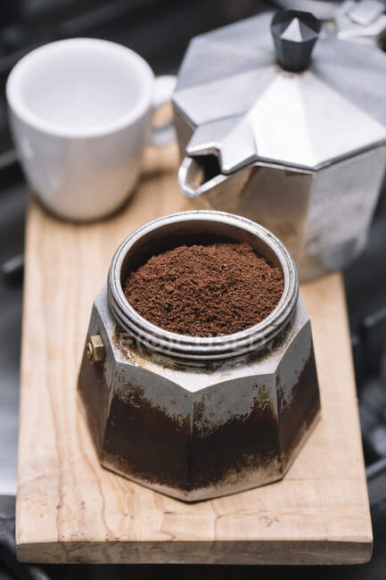 Vista de alto ângulo de café moído com recipiente com copo e fabricante em bandeja de madeira na cozinha — Fotografia de Stock