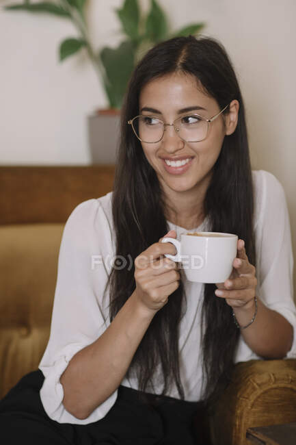 Lächelnde junge Frau mit einer Tasse Kaffee im Sessel in einem Café — Stockfoto