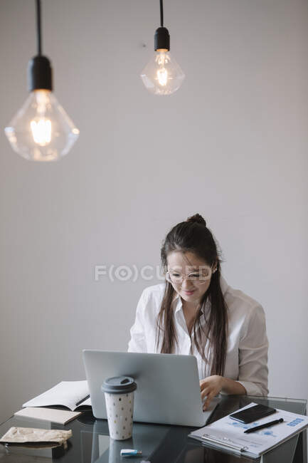 Giovane donna che lavora a tavola in ufficio utilizzando il computer portatile — Foto stock