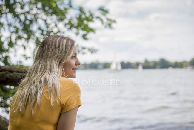Mulher sorridente sentada na margem do lago — Fotografia de Stock