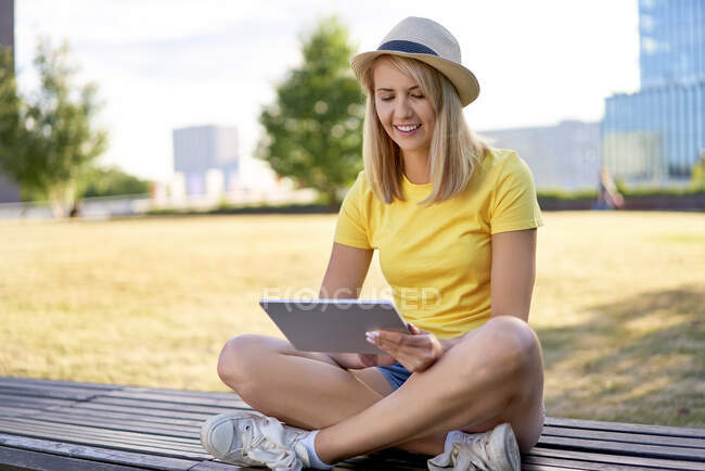 Jeune femme souriante assise sur un banc en ville à l'aide d'une tablette — Photo de stock