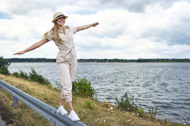Mulher feliz equilibrando na barreira de acidente ao lado do lago — Fotografia de Stock