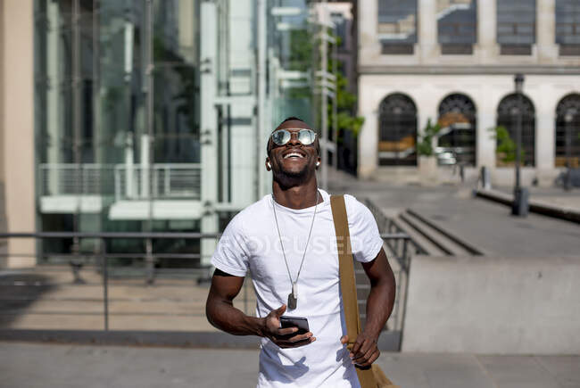 Smiling young man using smartphone and ear phones — Stock Photo