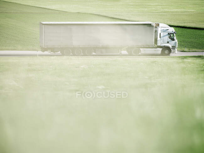 Camión moviéndose por carretera a lo largo del campo verde - foto de stock