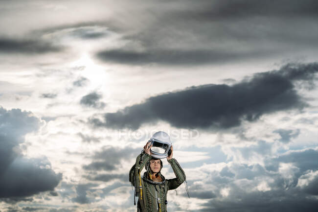 Homem posando vestido como um astronauta em um prado com nuvens dramáticas no fundo — Fotografia de Stock