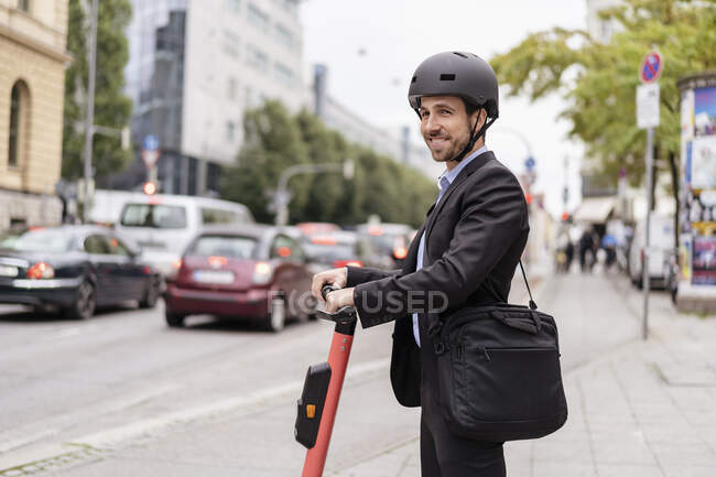 Lächelnder Geschäftsmann mit E-Scooter in der Stadt — Stockfoto