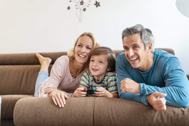 Genitori felici con figlio che giocano al videogioco sul divano a casa — Foto stock