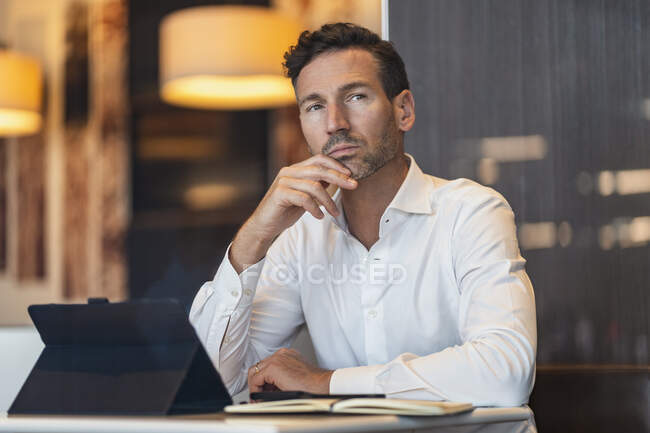 Uomo d'affari con tablet e notebook in un caffè pensando — Foto stock