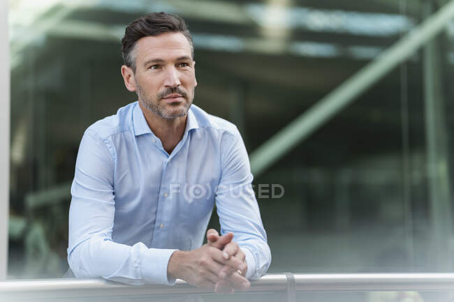 Businessman in the city leaning on railing — Stock Photo