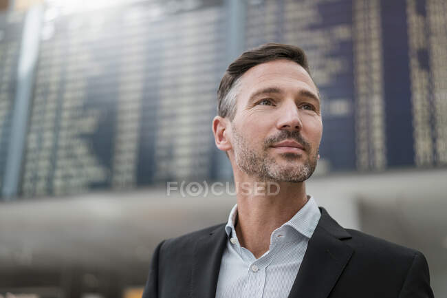 Portrait of businessman at arrival departure board at the airport — Stock Photo