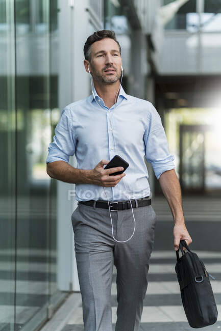 Uomo d'affari con cellulare e auricolari in movimento — Foto stock